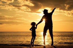 Father and son playing on the beach at the sunset time. Concept of friendly family.